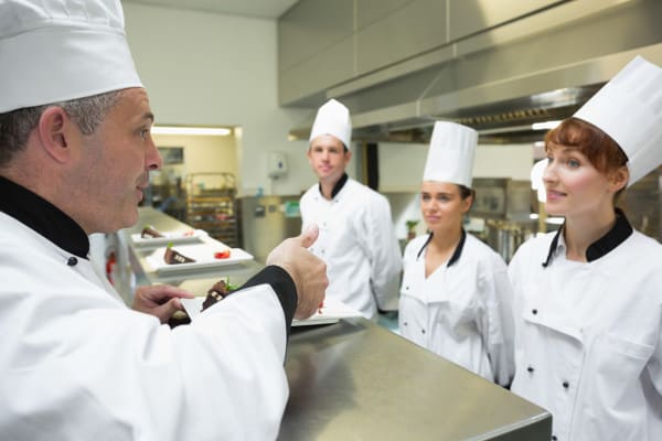 Head chef rating the plate of one of his apprentices in a kitchen
